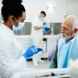Dentist in white coat and blue gloves showing patient sample dentures