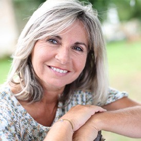 woman sitting outside with a beautiful smile thanks to dental implants
