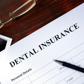 Dental insurance paperwork on top of dental X-rays, some dollar bills, with a pen and glasses scattered nearby