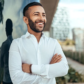 Bearded man in white shirt smiling with arms folded