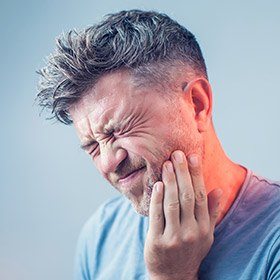 Grimacing man holding jaw in pain