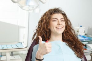 smiling young woman giving a thumbs up in the dentist’s chair