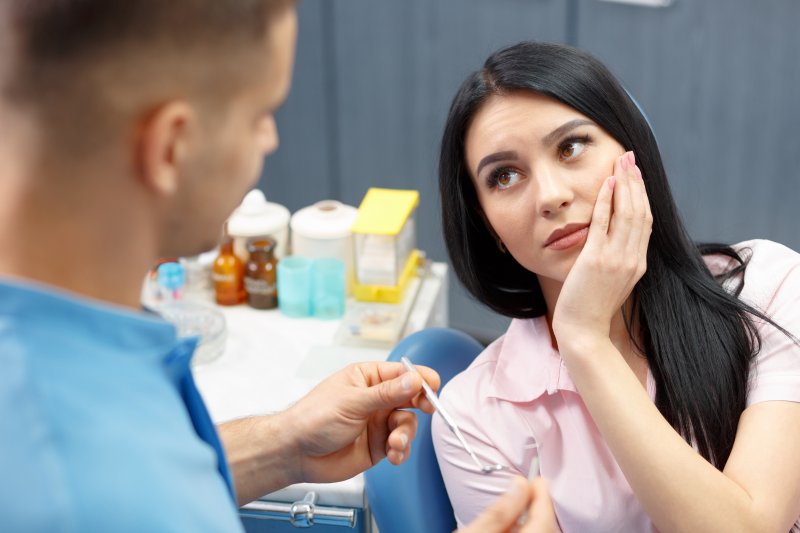 Woman holding cheek while looking at dentist