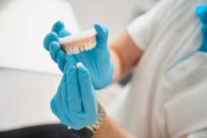 Dentist holding model of mouth with crown shown in other hand.